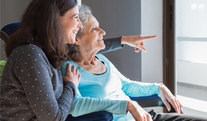 Younger woman holding older women while looking out the window.